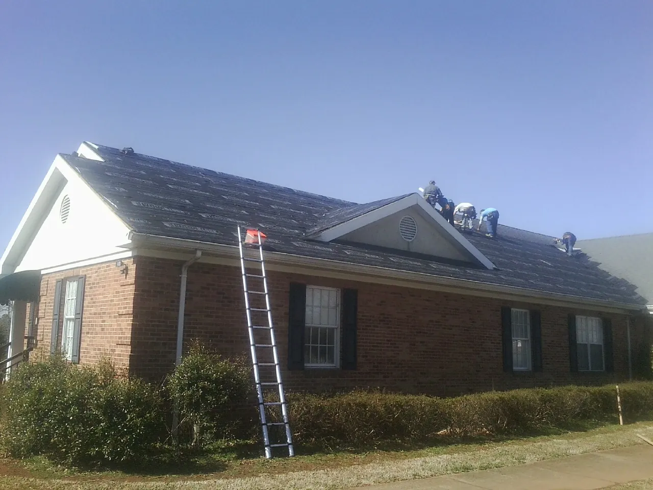 Crew tearing shingles off a brick ranch roof with a ladder set — Metal Roof Repair work by our crew in Fostoria