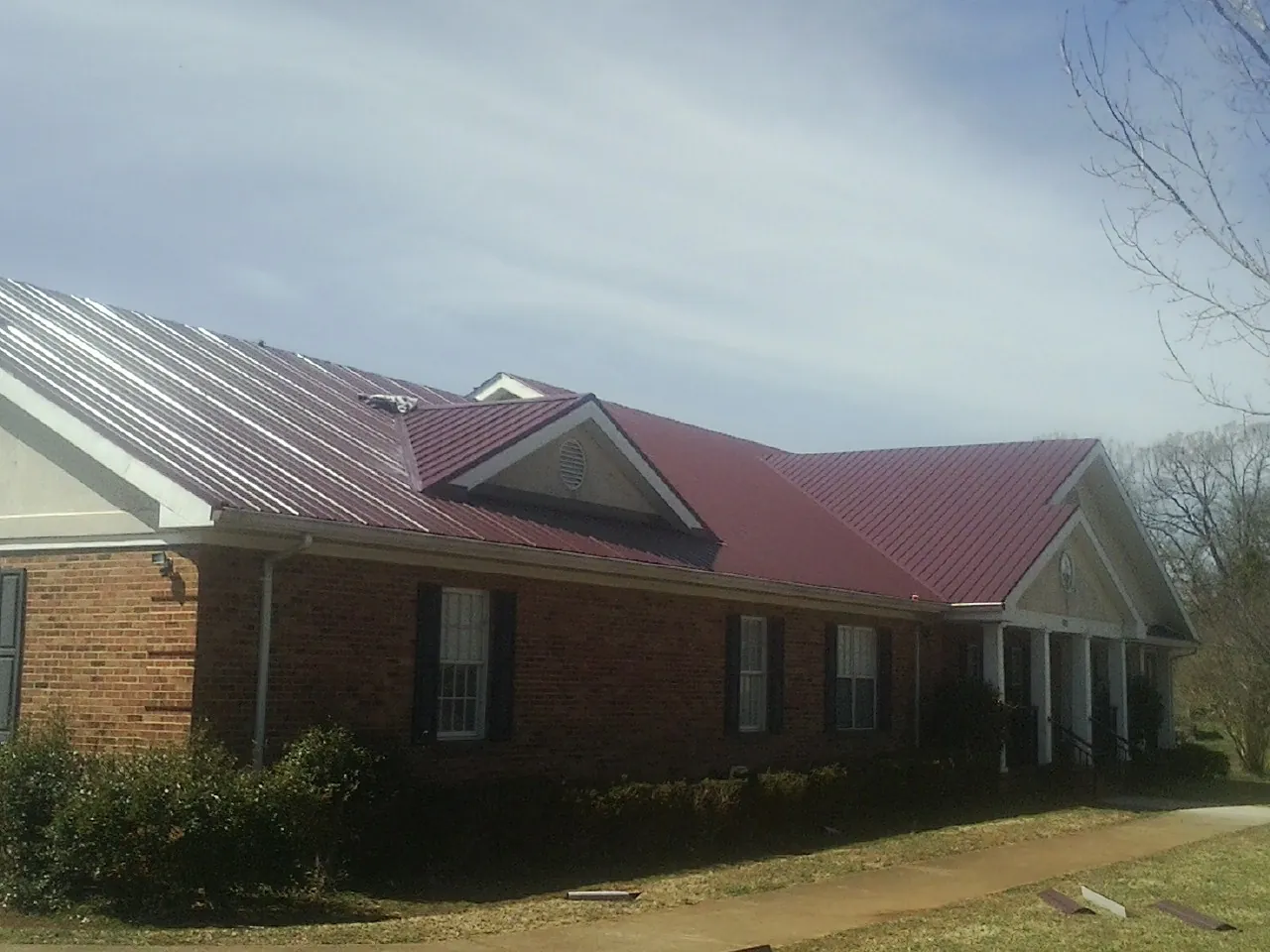 Red metal roof with gabled entries on a long brick building, from a Hail Damage Roof Repair job in Fostoria