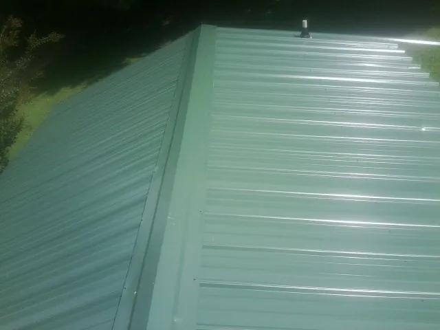 New green metal panels meeting at the ridge of a roof — Flat Roof Repair work by our crew in Fostoria