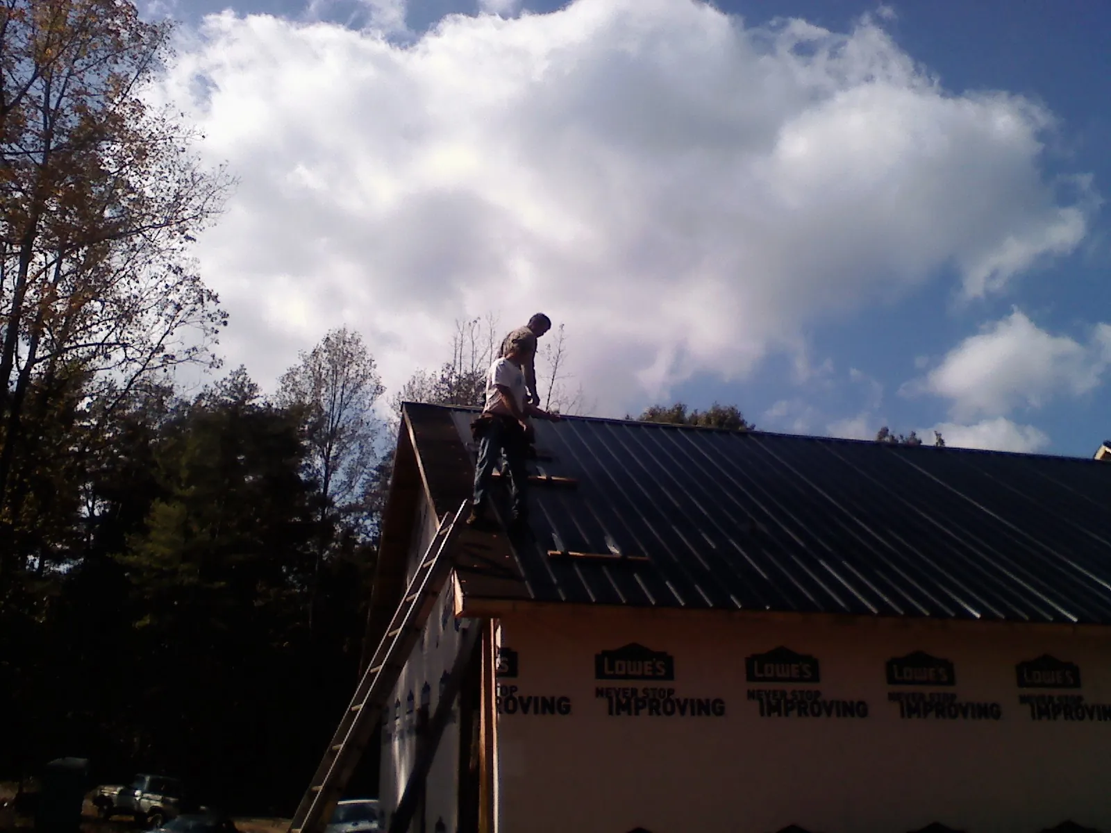 Roofer fastening dark metal panels high against a cloudy sky, from a Roof Inspection job in Fostoria