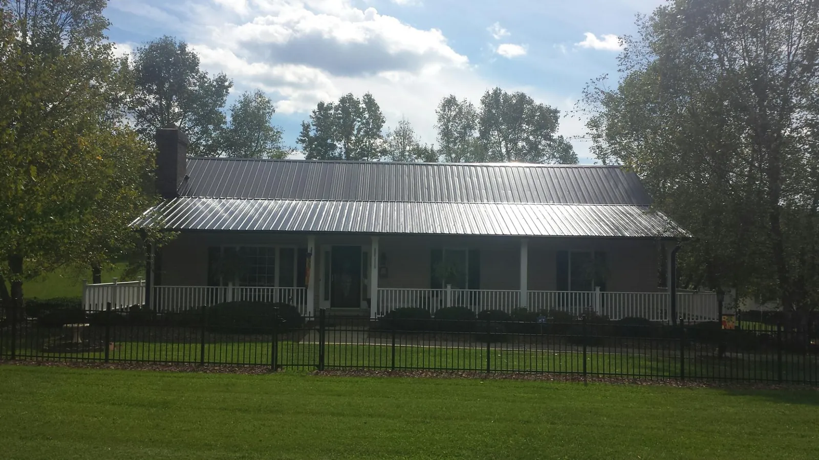 Gray metal roof on a brick ranch with a full width front porch — Gutter Guard Installation work by our crew in Fostoria